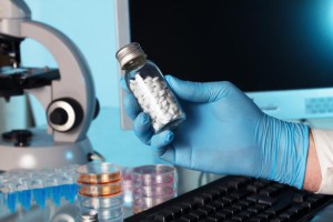 hand of a pharmacist holding a bottle of pills in a lab with blue background